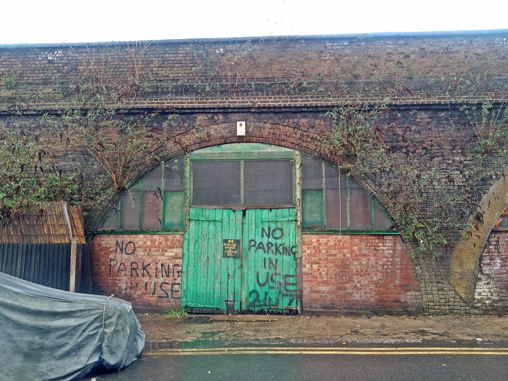 Dilapidated green doors with no parking painted on them under Brixton railway arch in South London
