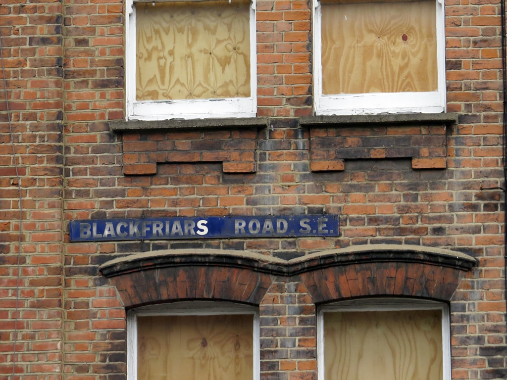 Boarded up Edwardian block with ancient blue and white Blackfriars Road sign on brick wall