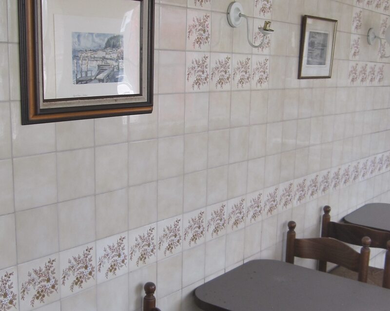 Derelict café interior showing beige tiles, table, chairs and photographs on the wall.
