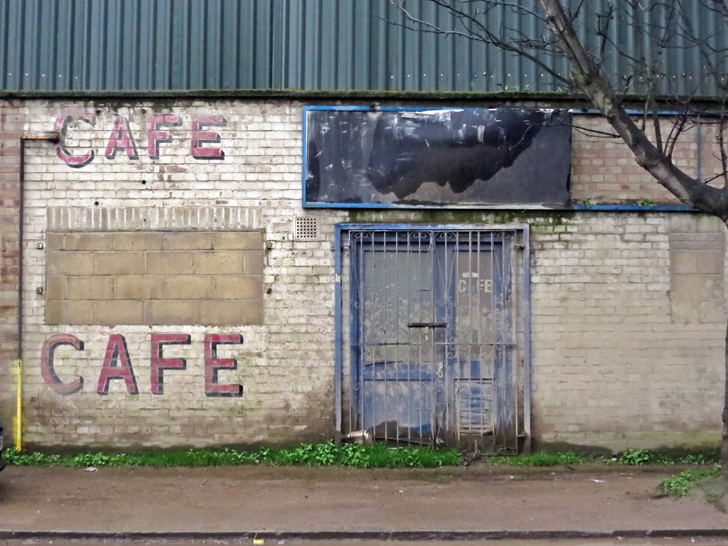 Bricked up window and metal grille over door of derelict cafe in Charlton, South London