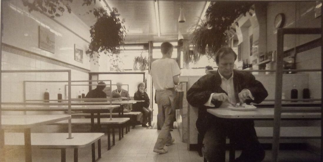 Actor Dennis Waterman sitting at a cafe table eating a meal from the Dennis Waterman in the East End book by Terry Green