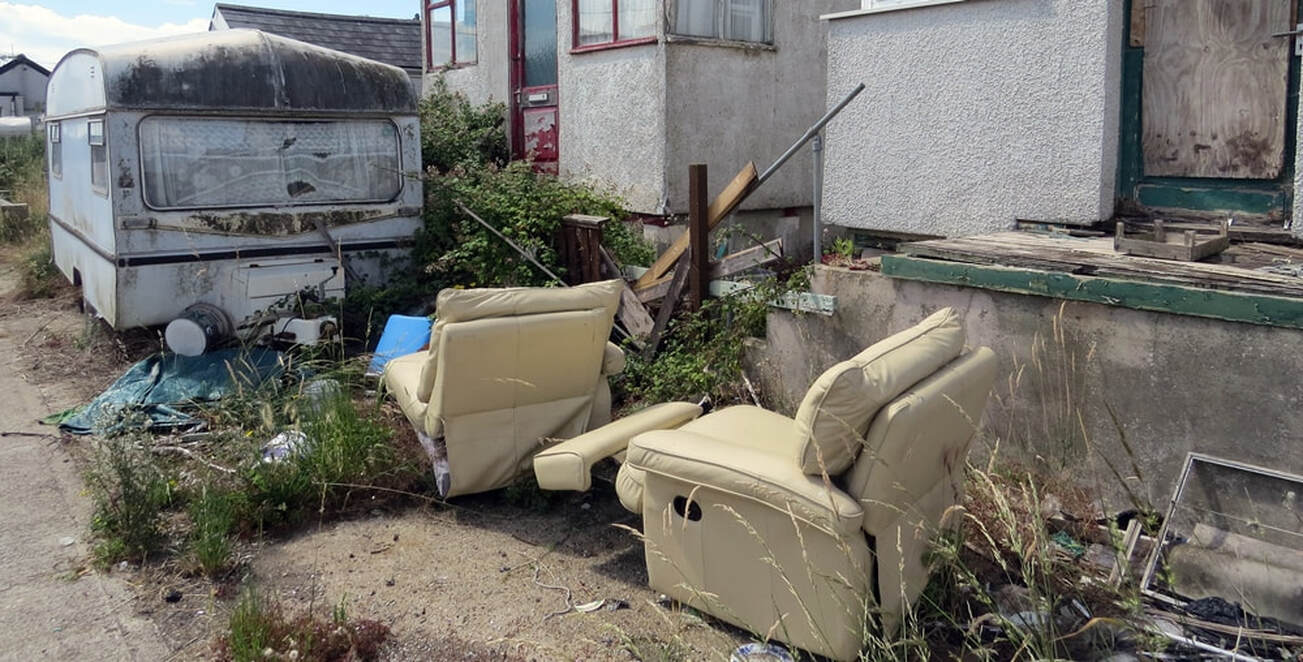 Picture of decaying caravan and abandoned sofas in front of dilapidated shacks in Jaywick, Essex