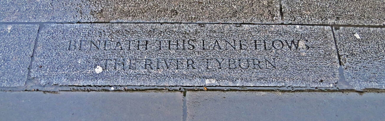 Engraved paving stone saying that London's lost River Tyburn flows under Marylebone Lane on Paul Talling's guided walking tour