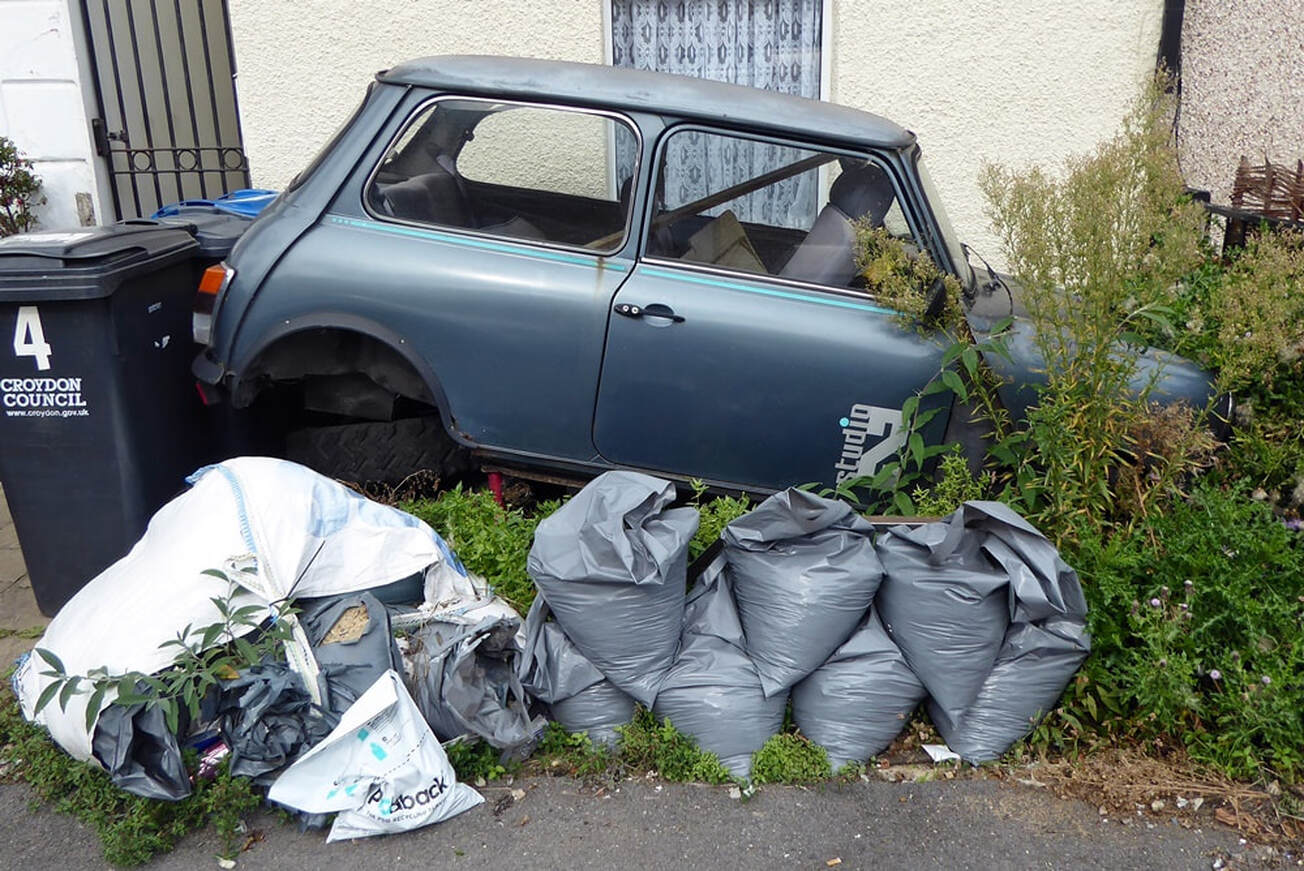 abandoned old style metallic grey Austin Mini in front garden surrounded by refuse sacks in South Norwood, London