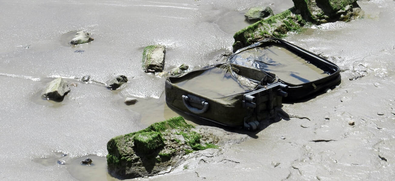 Abandoned suitcase full of water in the mud on the River Thames foreshore