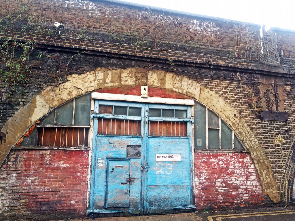 Blue boarded up garage doors under neglected railway arch in South London