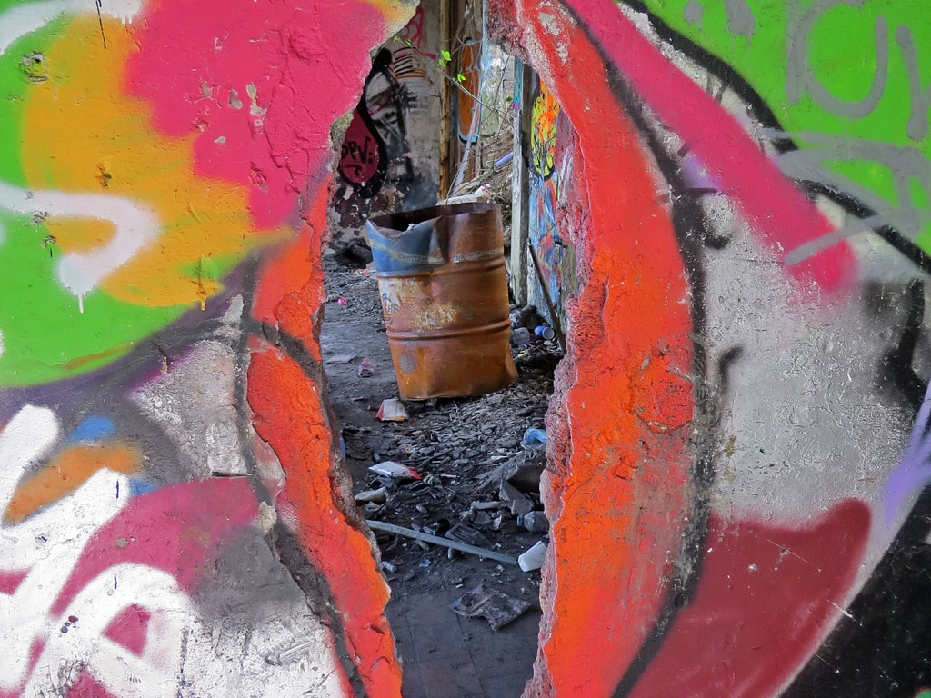 Abandoned oil drum viewed though hole in concrete wall of derelict building