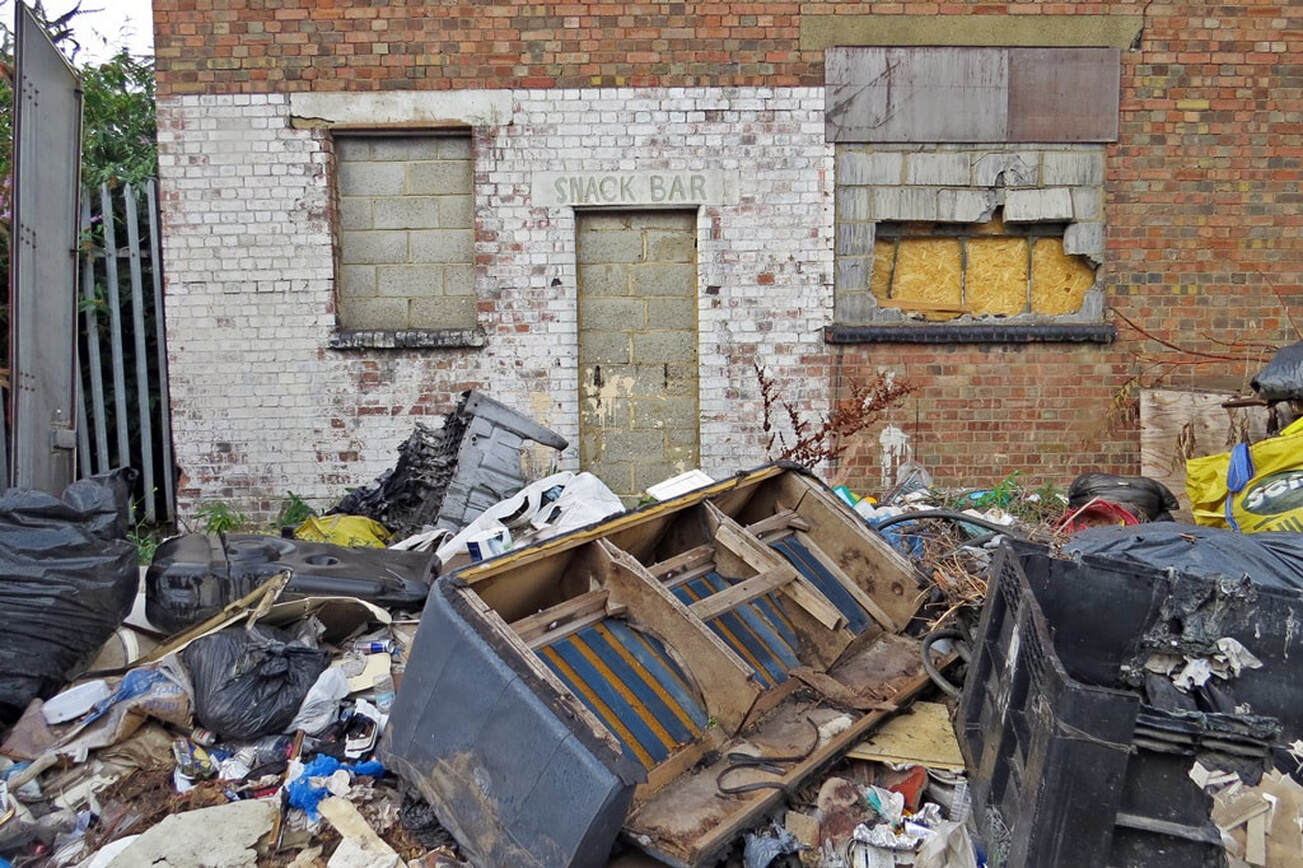 Picture of flytipped rubbish including a sofa in front of a derelict bricked up snack bar on industrial estate in East London
