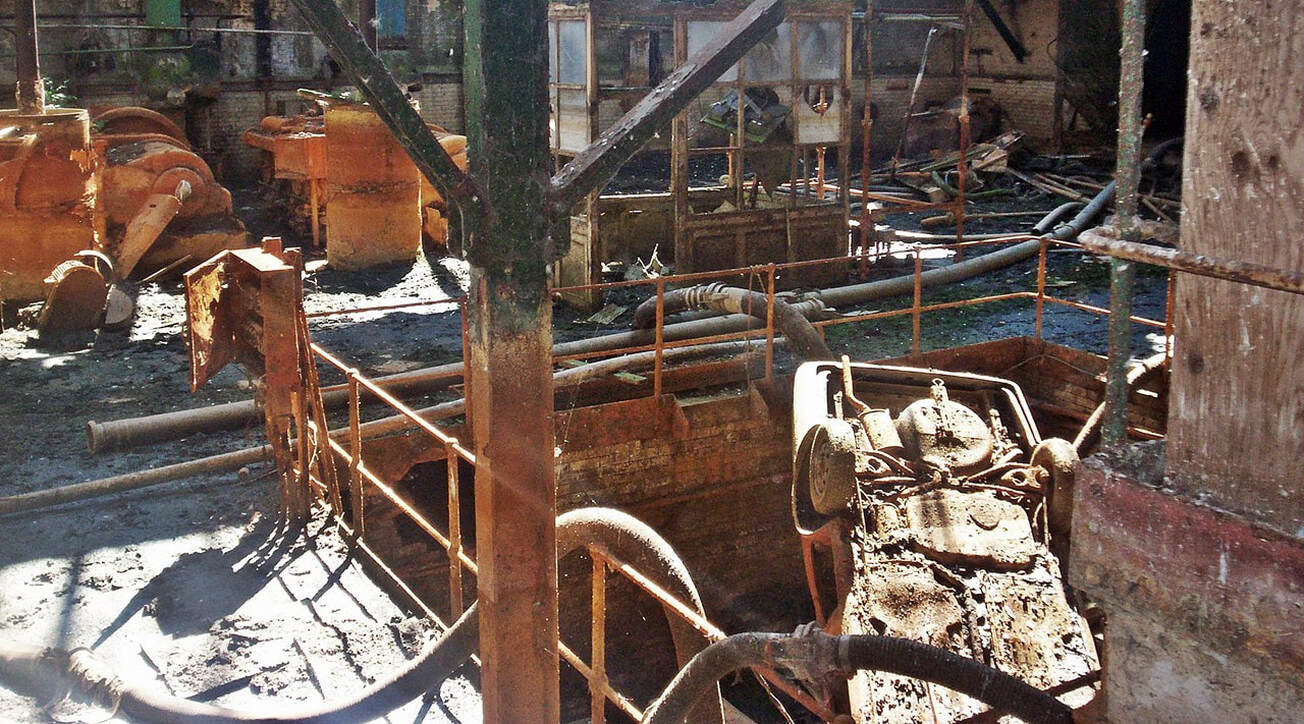 abandoned interior of derelict Victorian building at Beckton Sewage works with rusty abandoned equipment and an overturned vehicle 
