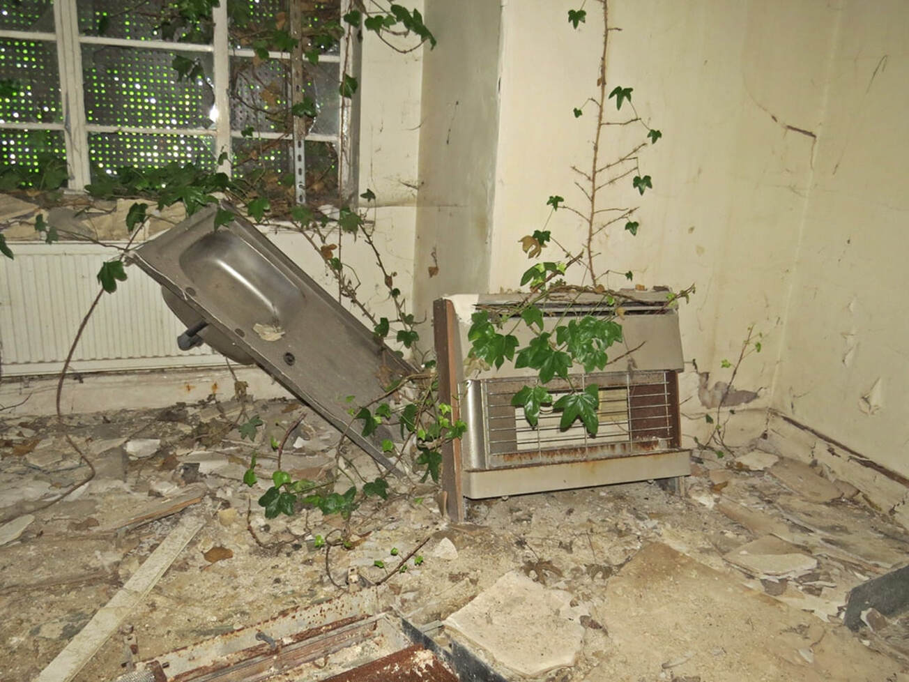 Abandoned gas fire and kitchen sink in derelict overgrown house at RAF Uxbridge in NW London