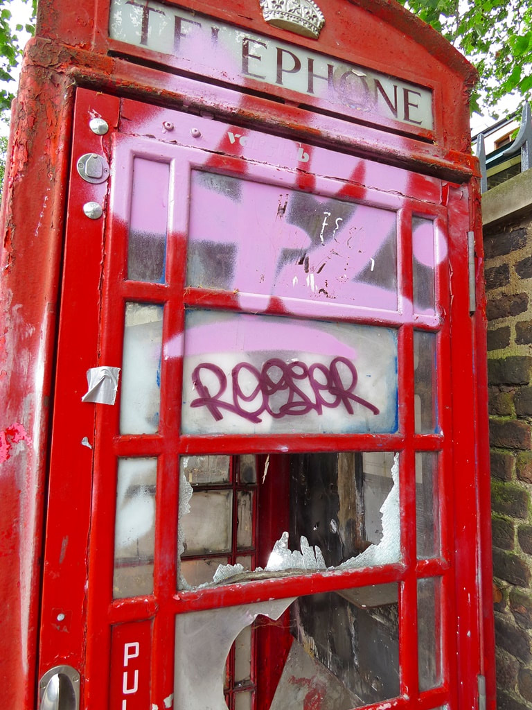 Red telephone box vandalised with pink spray paint and broken windows