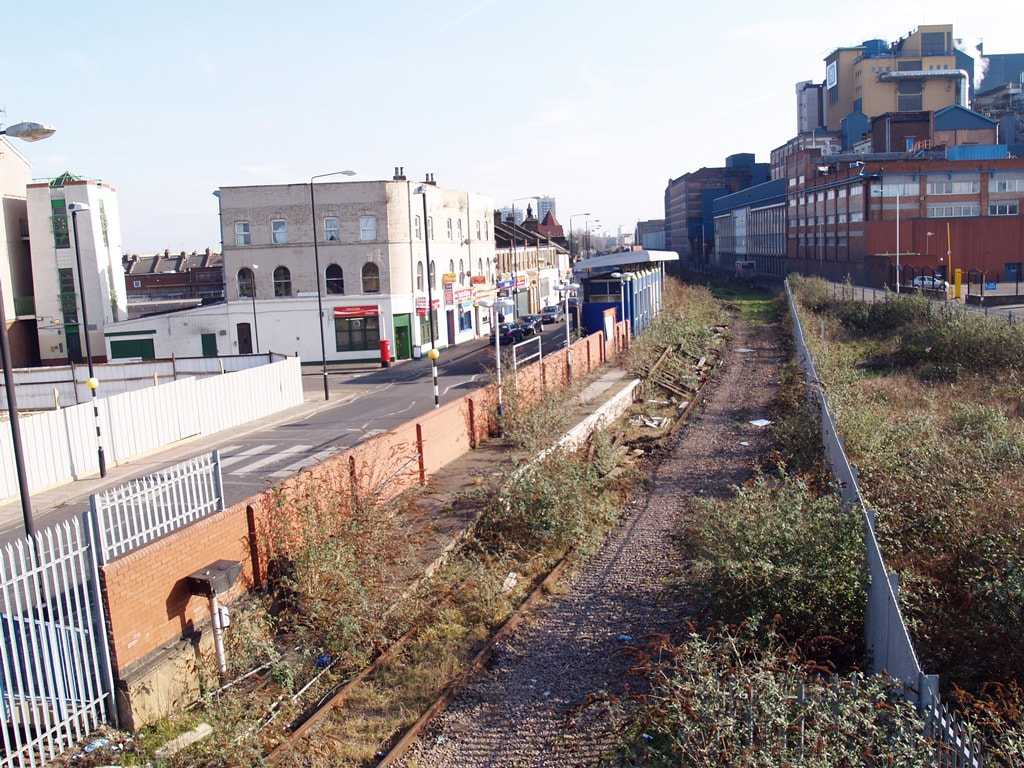 View of overgrown trackbed and derelict Silvertown station with Tate and Lyle factory to the right